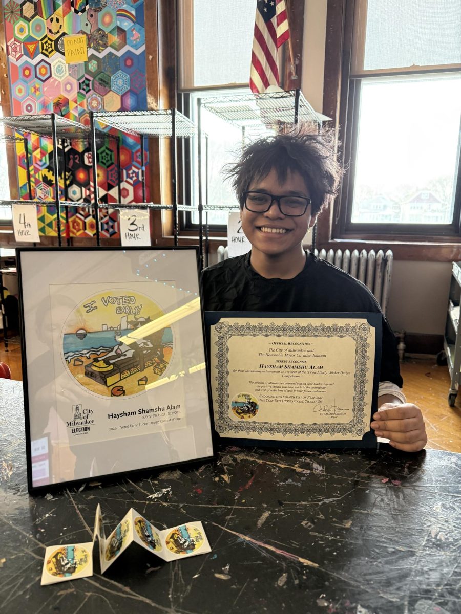 Haysham Shamshu Alam proudly displays his winning early voting sticker artwork alongside his official award from the City of Milwaukee, photographed in the art room at Bay View High School.

