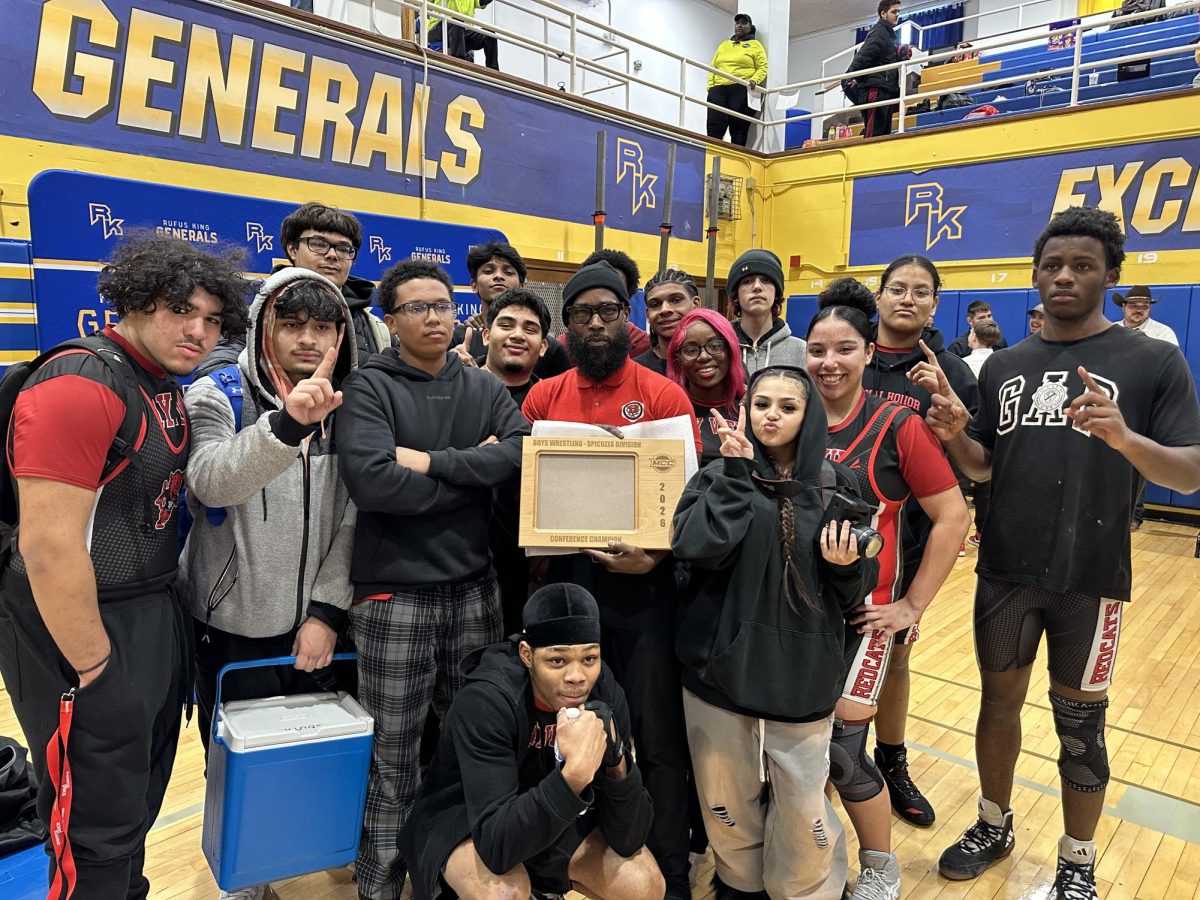Bay View boys wrestling coach proudly hoists the 2026 Milwaukee City Conference Spicuzza Division Championship trophy as his team gathers around, celebrating a hard-fought season and a title earned together.