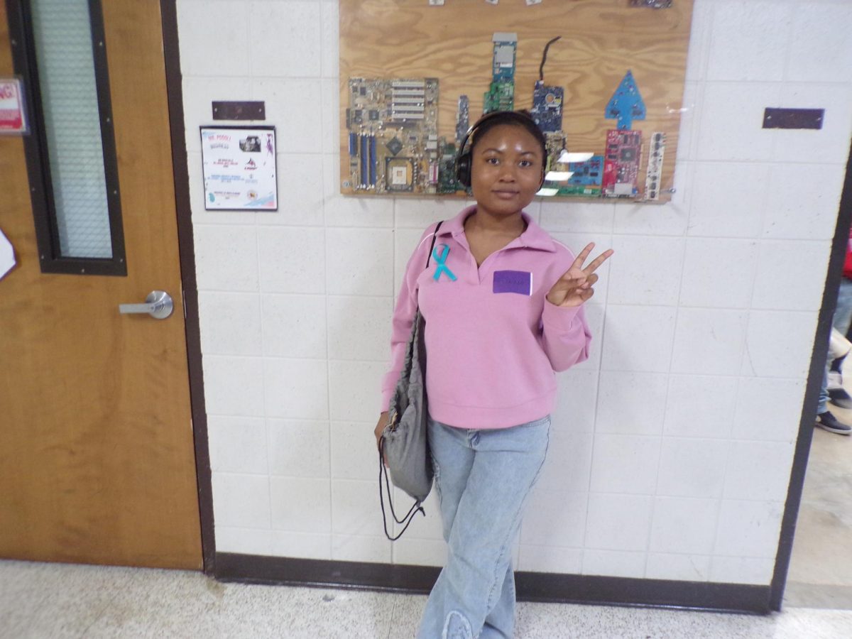 Student Sumiyiah Harris poses in the hallway during Denim Day, wearing jeans and a teal ribbon to raise awareness about sexual assault prevention and survivor support.